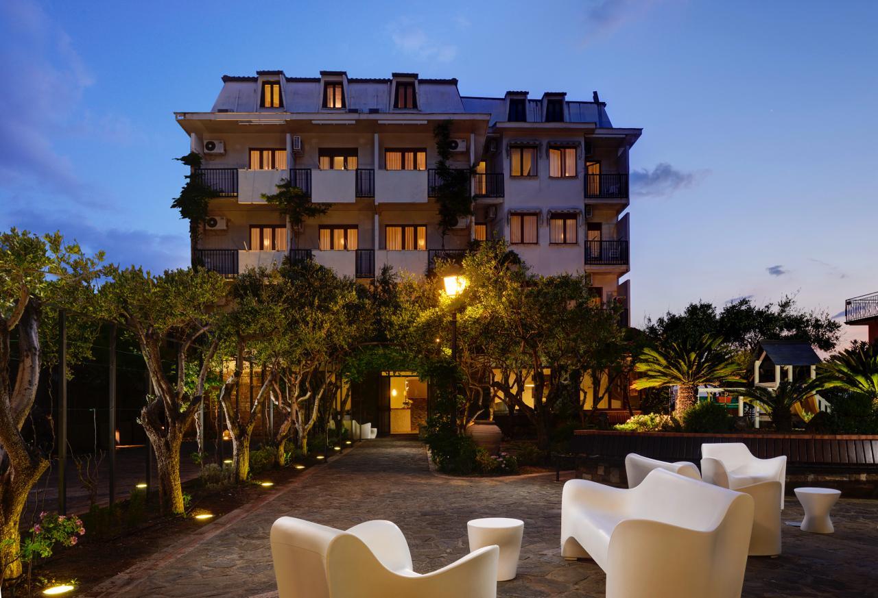 Hotel elegante al tramonto, con giardino illuminato e area relax all’aperto.
