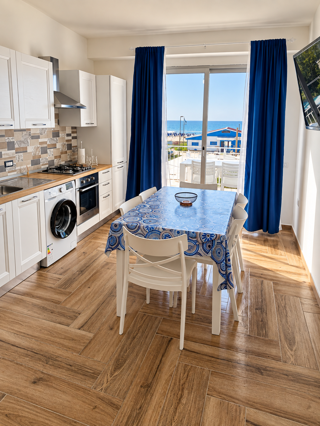 Cucina moderna vista mare con tavolo da pranzo e tende blu.