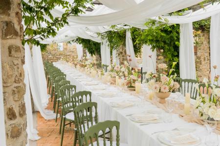 Outdoor wedding table in an elegant stone location, with sage green chairs, fresh flowers and white drapes under the pergola.