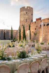 Elegant wedding setup in a historic courtyard, featuring decorated tables, Provençal-style chairs and floral arrangements in natural tones, at the foot of a stone castle.