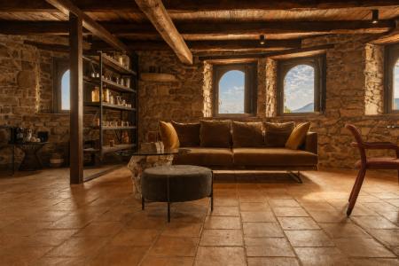 Rustikales Wohnzimmer mit freiliegenden Steinwänden, Holzbalken, Terrakottaboden und braunem Ledersofa, das durch das natürliche Licht der Panoramafenster erhellt wird.