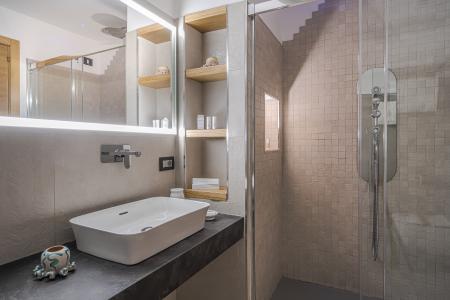 Modernes Badezimmer mit Aufsatzwaschbecken, hinterleuchtetem Spiegel, ebenerdiger Dusche mit Steinoptik-Wandverkleidung und Holznischen.