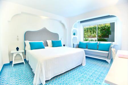 Camera da letto luminosa con letto matrimoniale, testiera grigia, dettagli turchesi e pavimento decorativo.