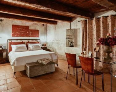 Elegant-rustikales Schlafzimmer mit freiliegenden Holzbalken, Terrakottaboden, Doppelbett mit weißer Bettwäsche und Möbeln in warmen Farbtönen.