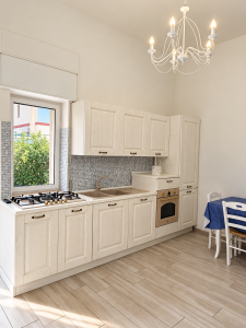 Cucina luminosa e moderna con mobili bianchi, piano cottura, forno, lavello e tavolo da pranzo.