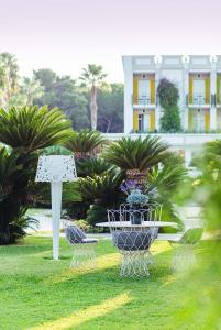 Giardino elegante con tavolo e sedie bianche in ferro battuto, palme e vegetazione rigogliosa.