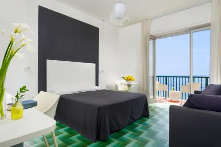 Camera da letto moderna e luminosa con letto matrimoniale, arredi eleganti, ampia vetrata e vista sul mare.