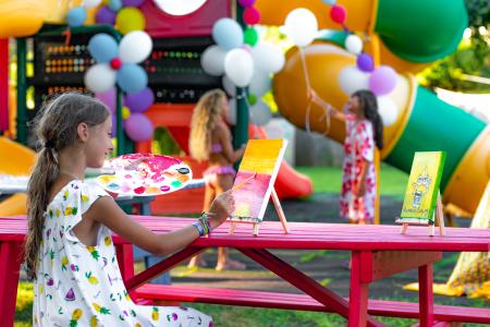 Bambina dipinge su una tela durante una festa per bambini colorata con palloncini e giochi gonfiabili.