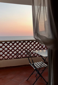 Balcone vista mare al tramonto, con tavolino e sedie affacciati sull’orizzonte.