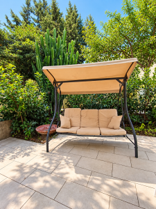 Altalena da giardino con struttura in metallo e cuscini beige, immersa nel verde.