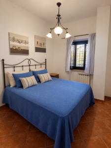 Camera matrimoniale con letto in ferro battuto, biancheria blu, comodini e finestra con tende, in stile rustico.