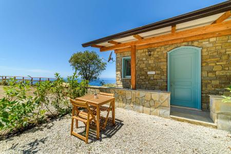 Esterno della Camera Enea con tavolo e sedie, immerso nella natura e con vista sul mare.